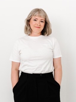 Marlene Goldmann steht vor einer hellen Wand, in weißem T-Shirt, die Hände in den Hosentaschen.